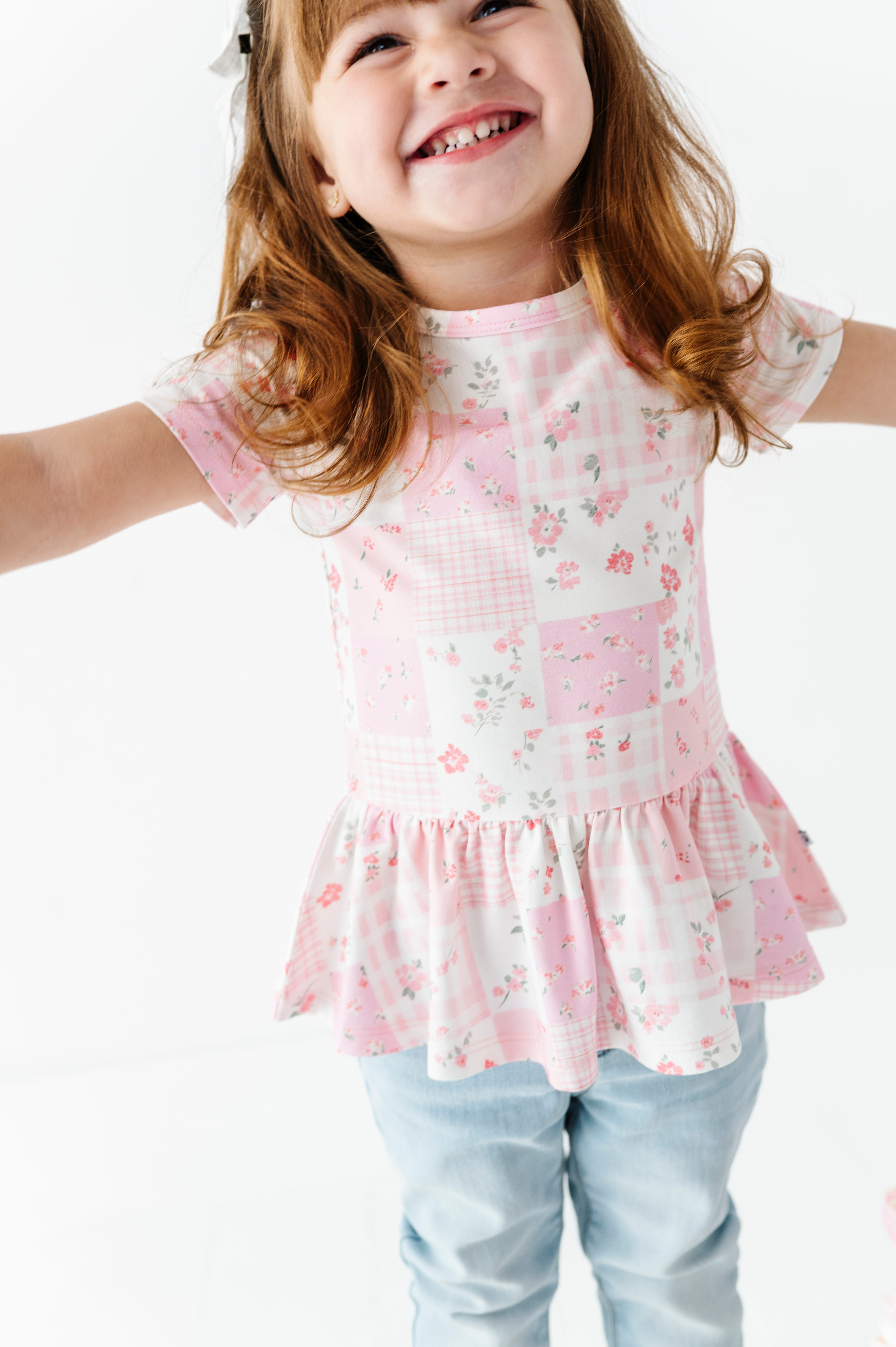 Child wearing a pink floral bamboo-cotton peplum blouse with ruffled details on a white background